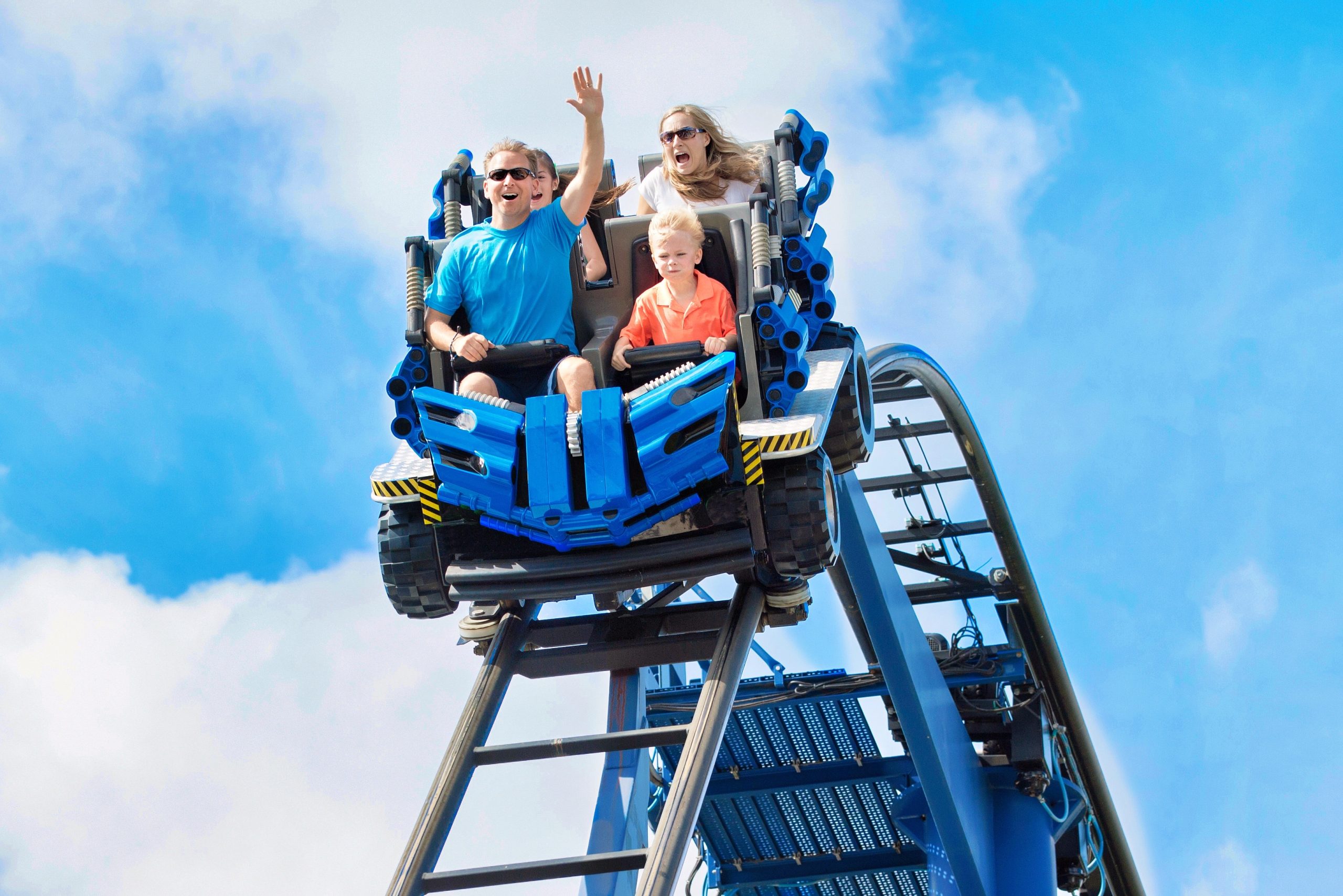Young family having fun riding a rollercoaster at a theme park. Screaming, laughing and enjoying a fun summer vacation together.