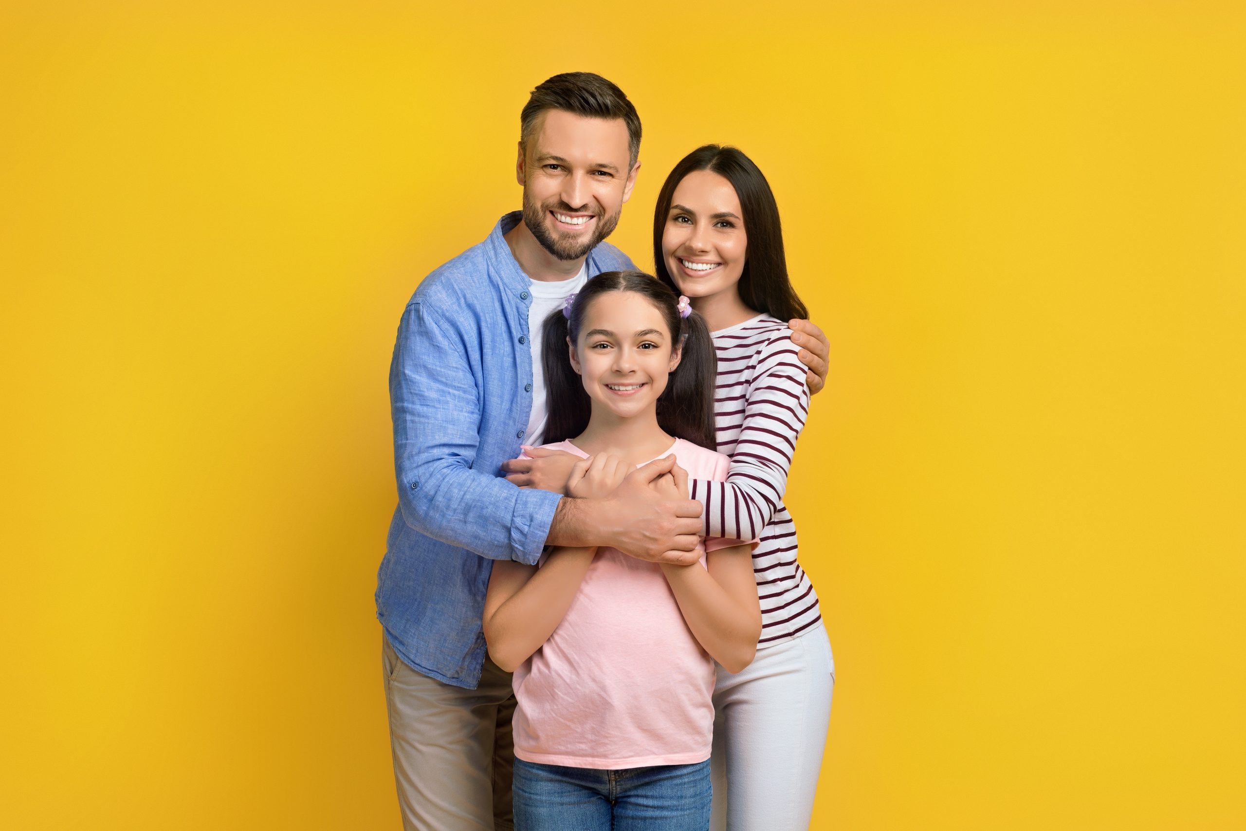 Closeup Portrait Of Happy Family Of Three With Teen Daughter, Joyful Young Parents And Their Teenager Female Child Embracing And Posing At Camera, Standing Over Yellow Studio Background, Copy Space